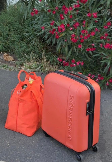 Organizer - den perfekte reisevesken: oransje kofferter og veske i et hageområde.