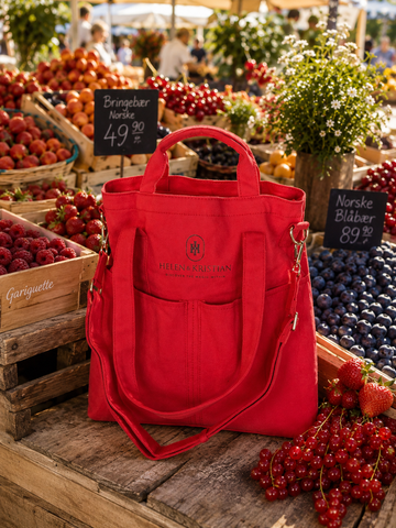 Rød totebag fra HELEN & KRISTIAN foran bær og frukt på et marked, perfekt for Organizer fargekolleksjon.