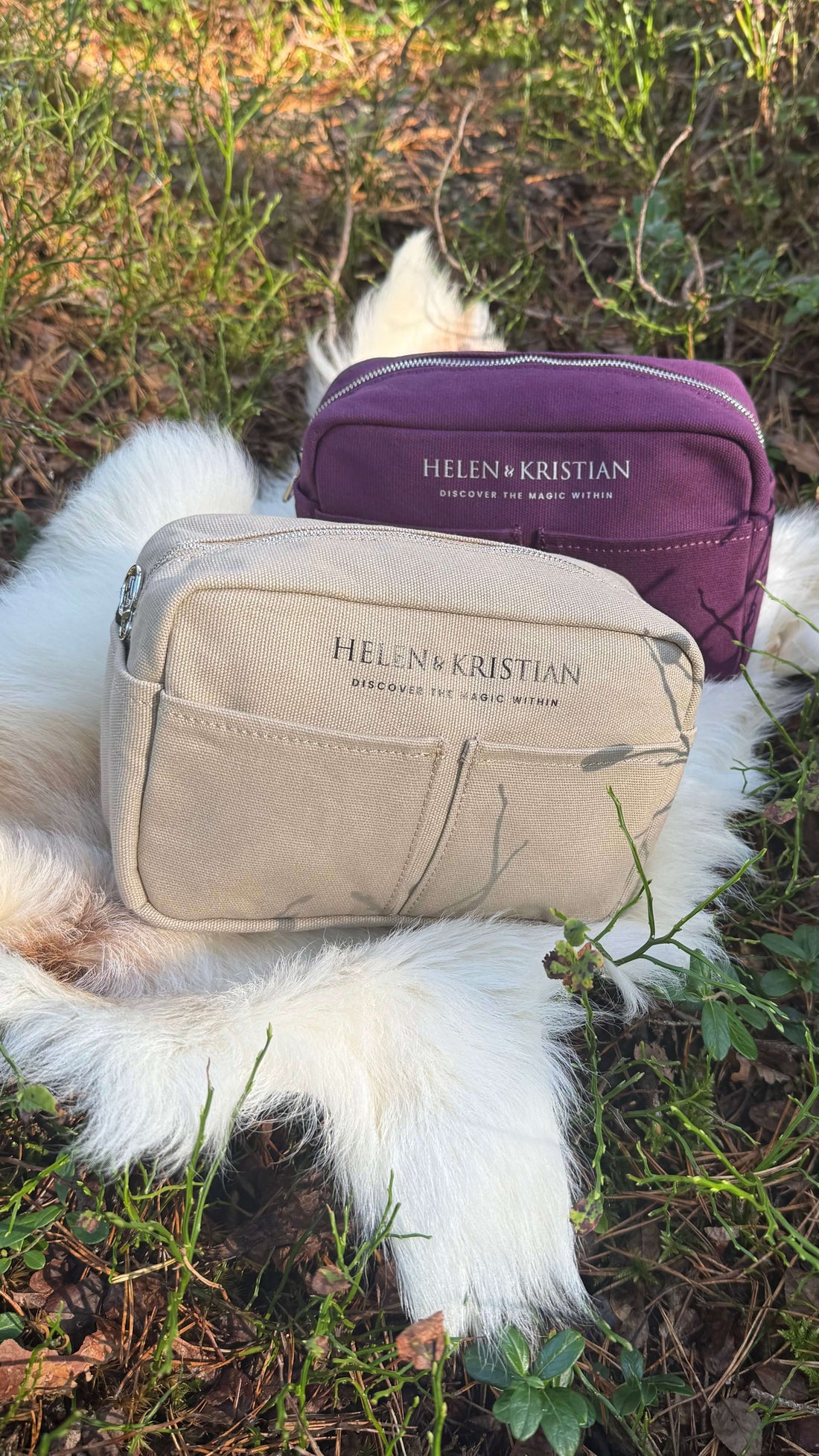 Two Helen & Kristian toiletry bags on a fur blanket, one in purple and one in beige, outdoors by a reflective lake.