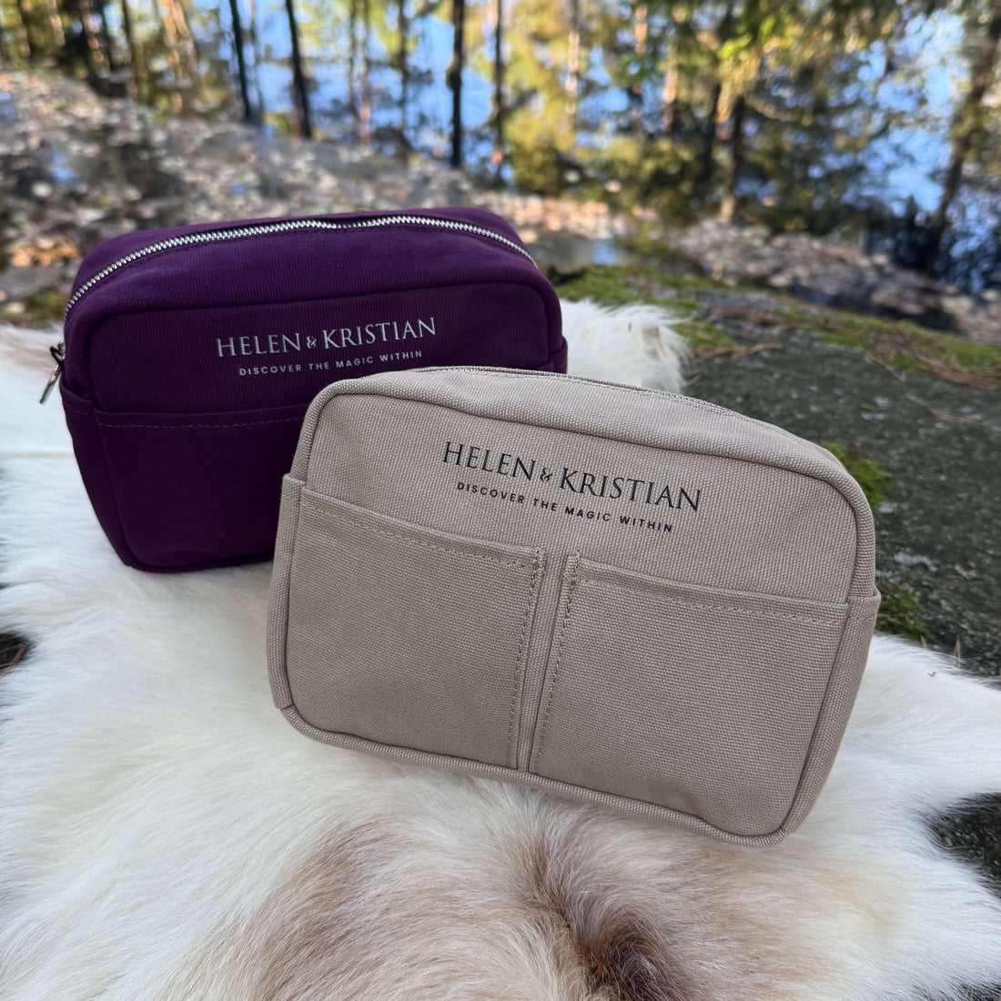 Two Helen & Kristian toiletry bags on a fur blanket, one in purple and one in beige, outdoors by a reflective lake.