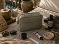Nesty - Stor Toalettmappe - Deep Forest laying on a textured surface surrounded by beauty products and sunglasses.