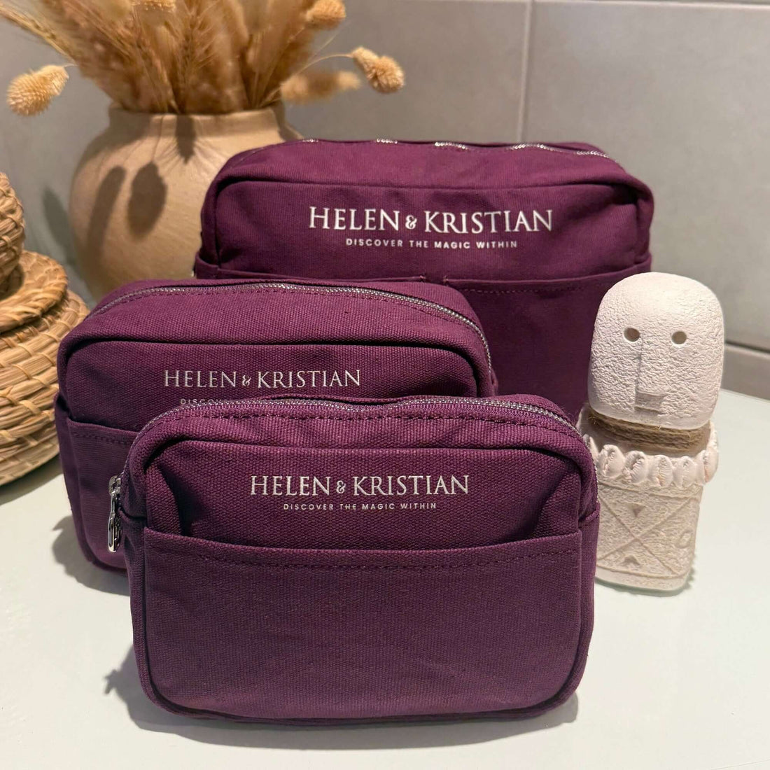 Purple cosmetic bag with 'Helen Kristian' branding on a wooden surface with a small pumpkin and plant in the background.