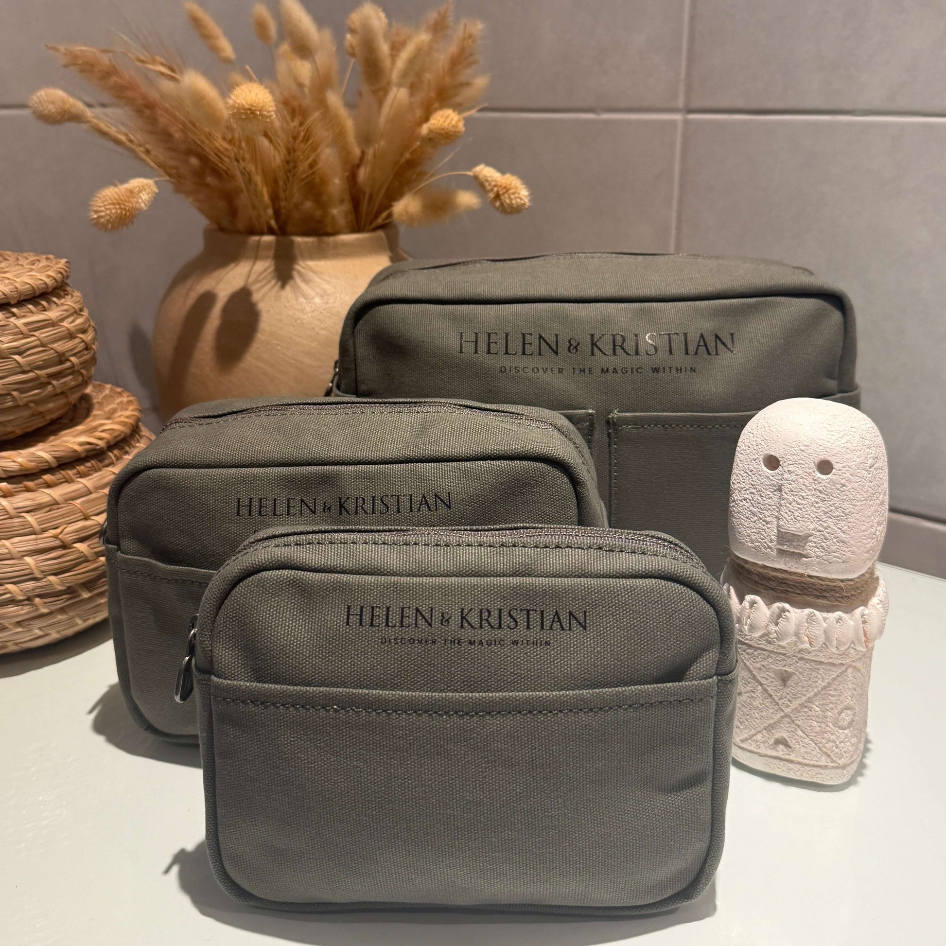 Set of green cosmetic bags with 'Helen & Kristian´ branding on a neutral background.