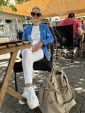 Person in blue blazer and white pants sitting at an outdoor café with a beige Viking Haze organizer bag on the ground.