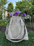 Beige Viking Haze organizer bag with purple flowers, featuring Helen Kristian logo, placed on grass amidst garden backdrop.